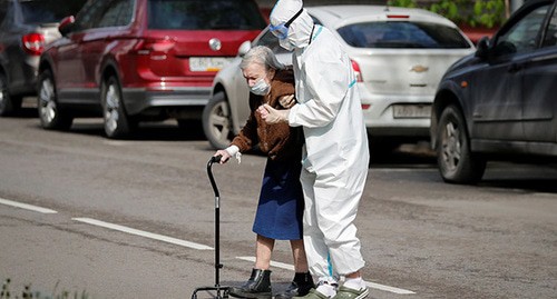 Медицинский работник в защитном костюме помогает пожилой женщине. Фото: REUTERS/Shamil Zhumatov